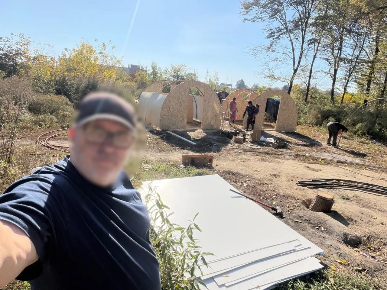 Adăposturi arcuite din lemn în construcție, într-o zonă cu vegetație